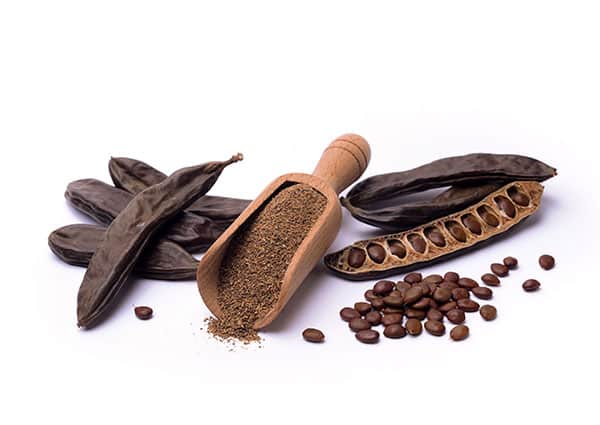 семена и брашно от рожков на бял фон с дървена лъжица